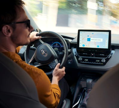 Muž v oranžovom svetri otáča práva, keď riadi vozidlo Toyota. Multimediálny systém vozidla zobrazuje aktualizáciu softvéru.